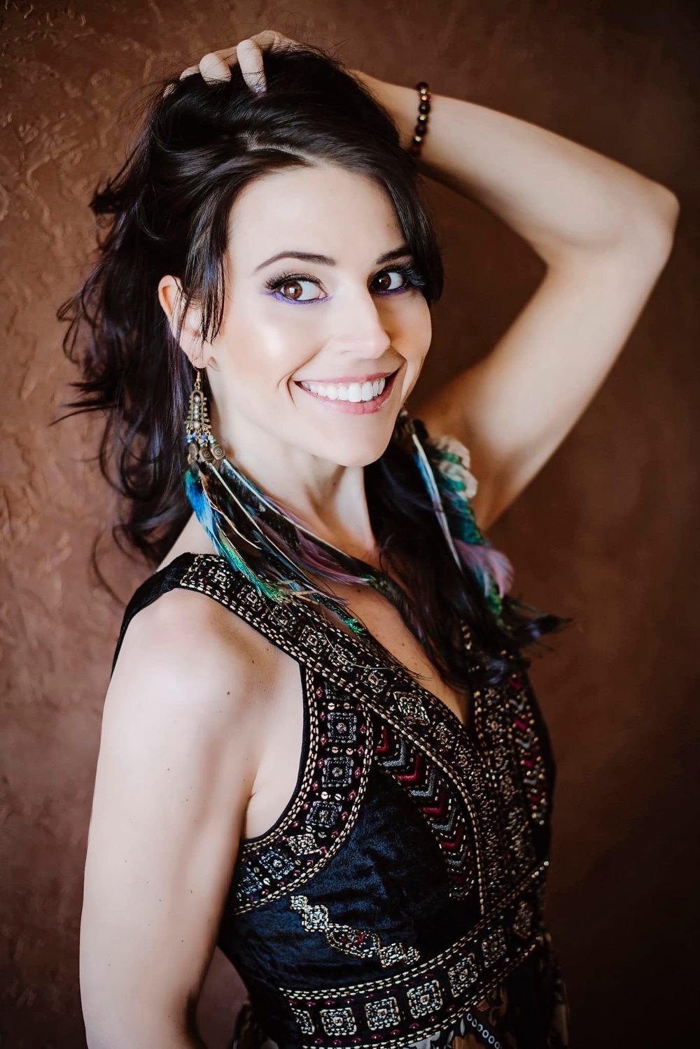 Solara Rose in a beaded black gown with feather earrings, smiling to camera