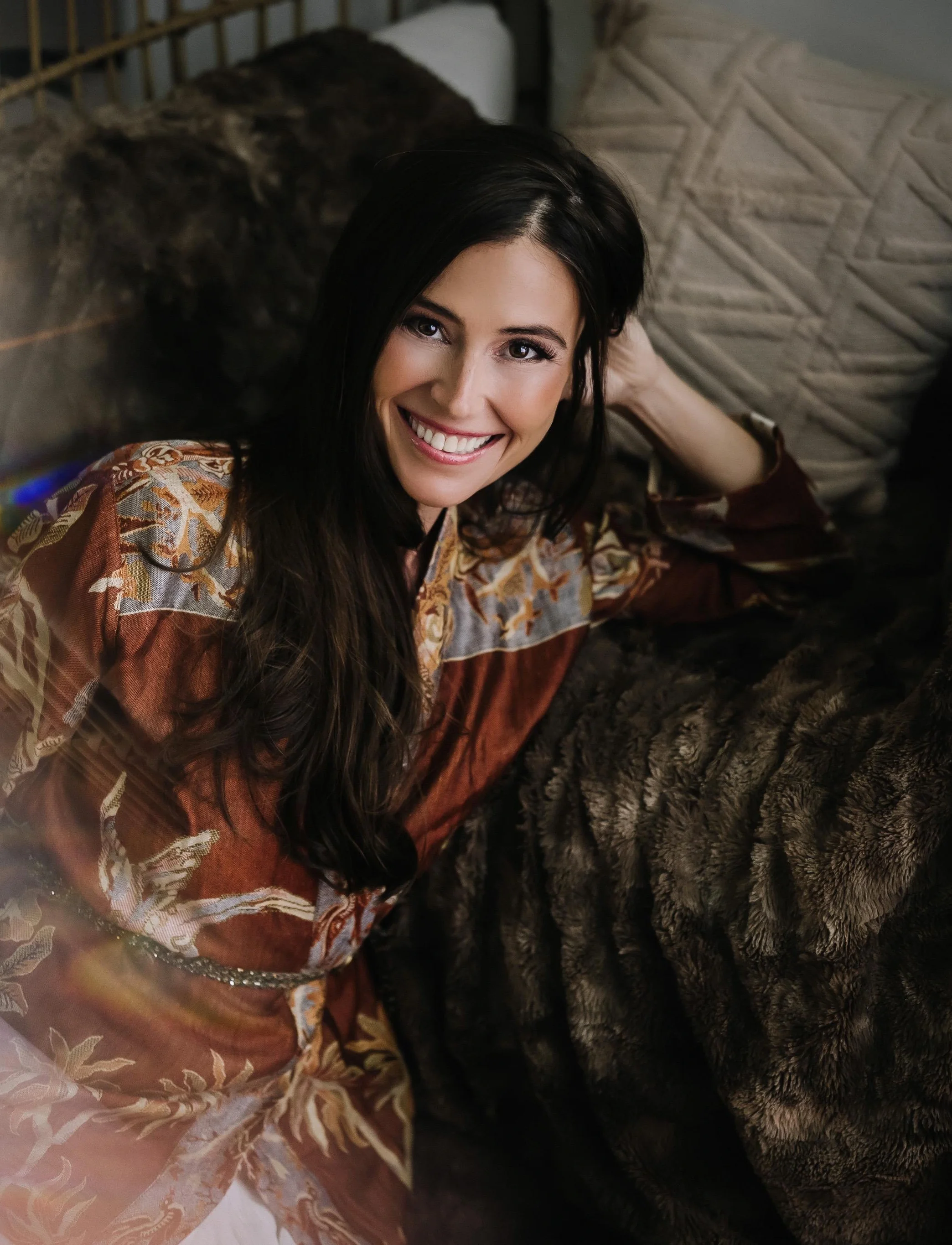 Solara Rose smiling warmly, reclining on a fur throw in a rust-coloured floral silk robe